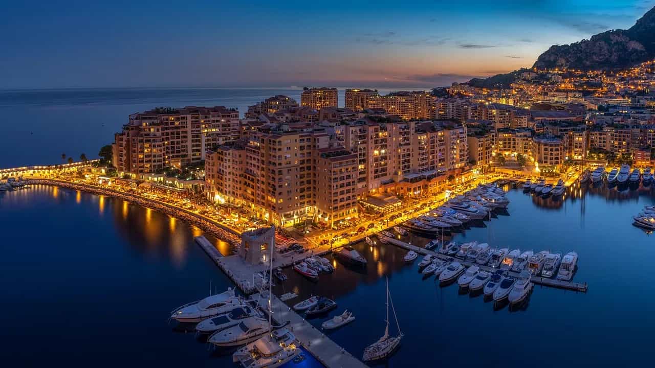 Monaco's harbour at dusk, yachts moored along the quay and the lit apartment buildings reflected in the water.