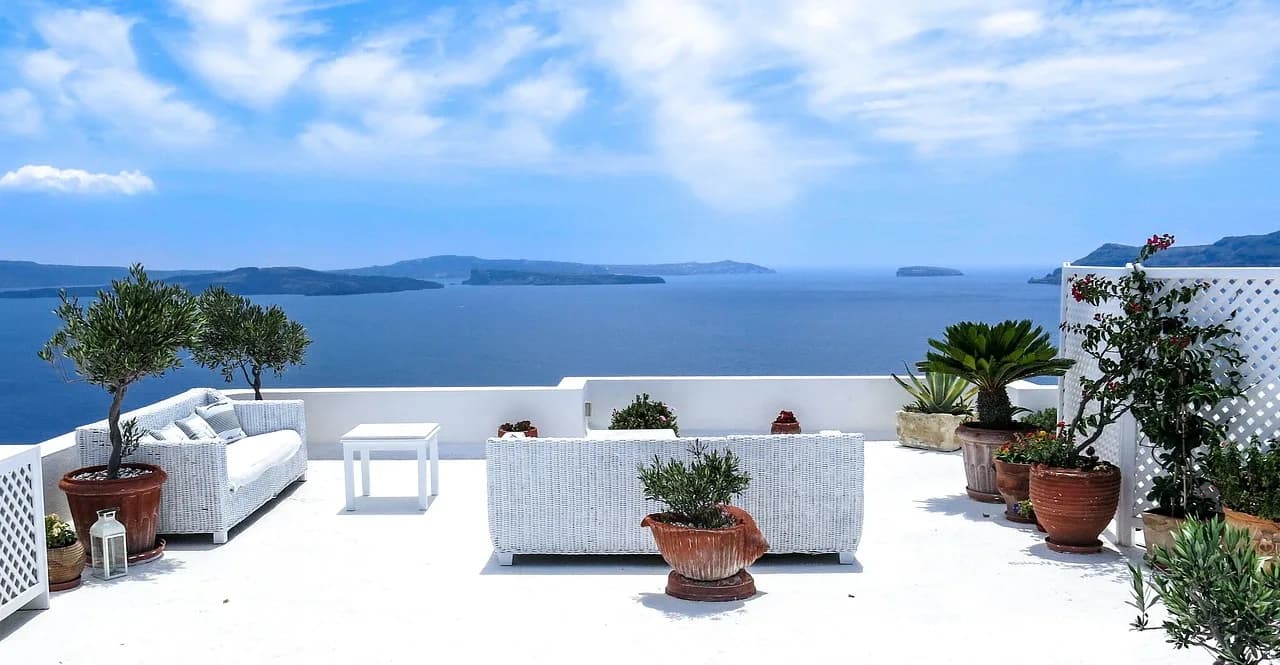 Një tarracë e bardhë qetësuese me pamje nga deti i thellë blu Egje dhe ishujt në largësi.