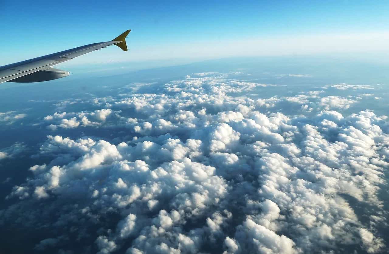 Krahu i një avioni fluturon mbi një det të gjerë reje nën një qiell blu të kthjellët.