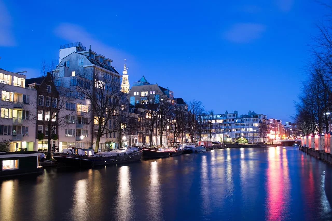 Kanali Amstel në orën blu, Amsterdam, Holandë – varka-shtëpi dhe shtëpi kanali të ndriçuara