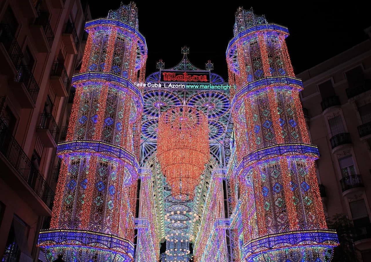 A street of towering light arches lit in red and blue for the Fallas festival in Valencia at night.