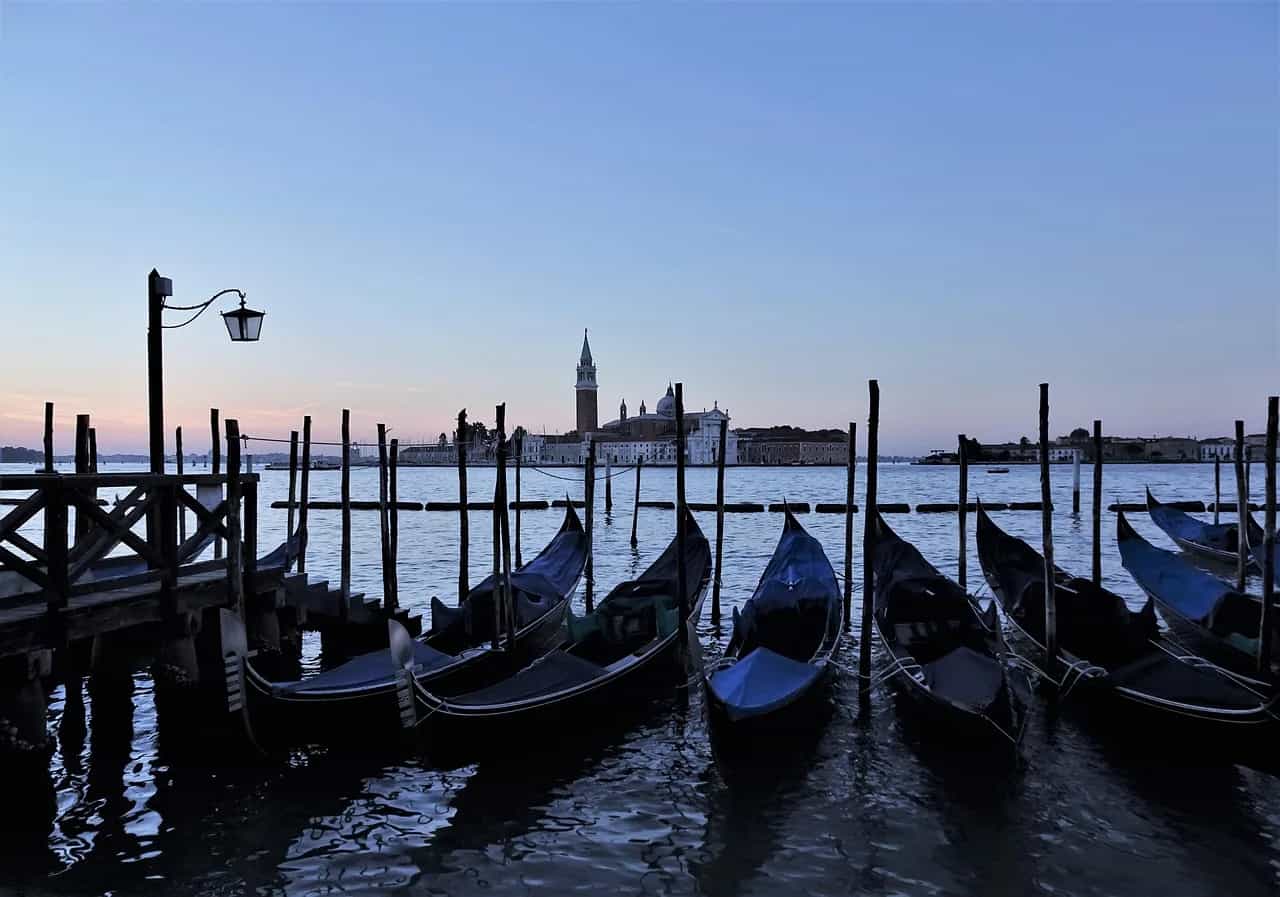 Gondolas moored at wooden posts in the Venetian lagoon at dusk, with San Giorgio Maggiore in the distance.