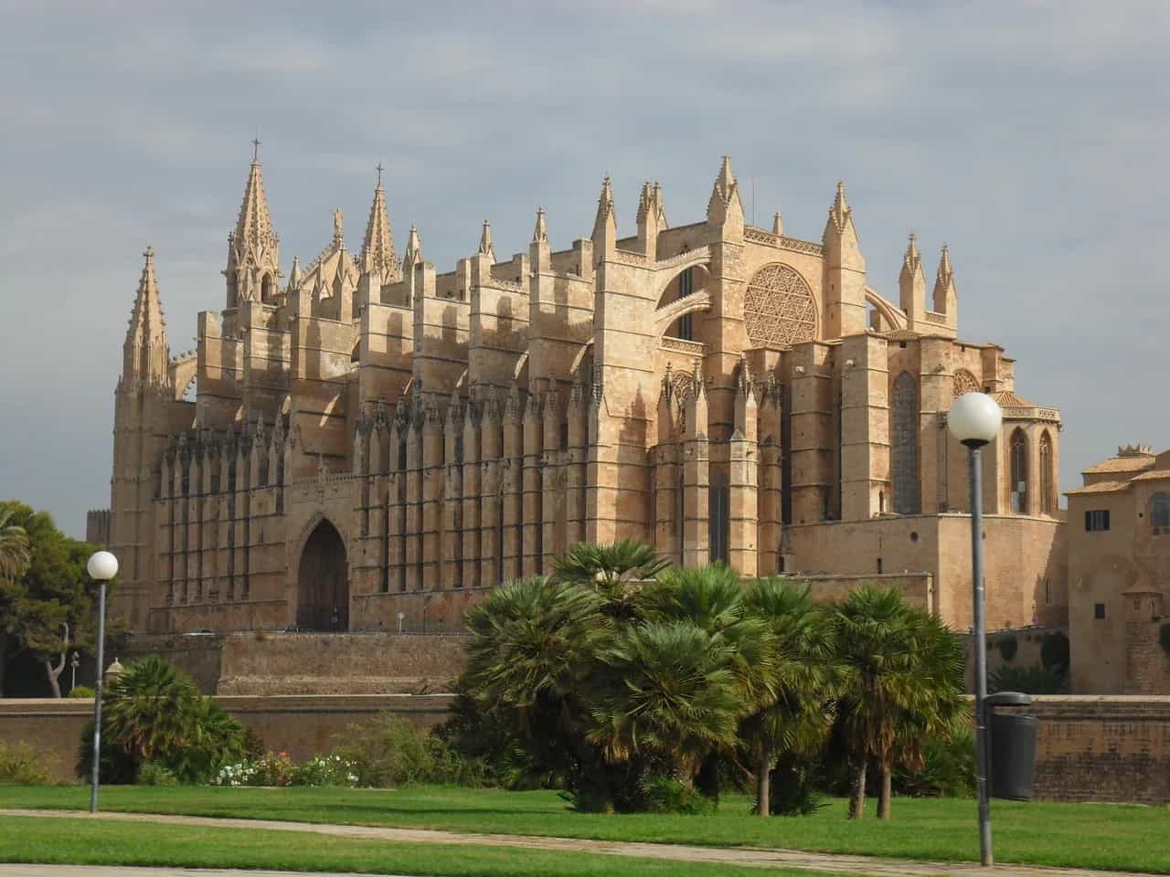 The sandstone Gothic cathedral of La Seu rising above palm trees and lawns in Palma de Mallorca.