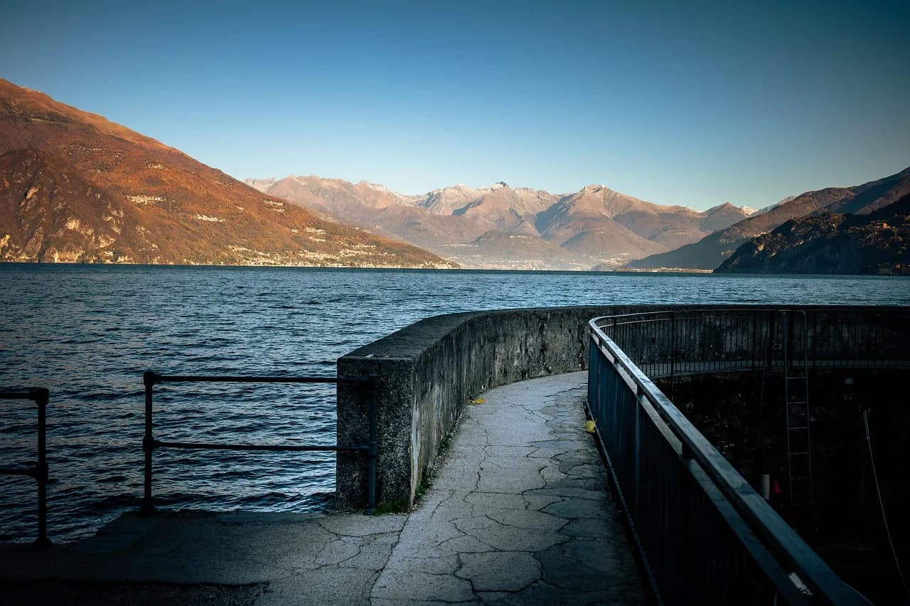 A stone lakeside promenade on Lake Como with snow-dusted mountains across the water.