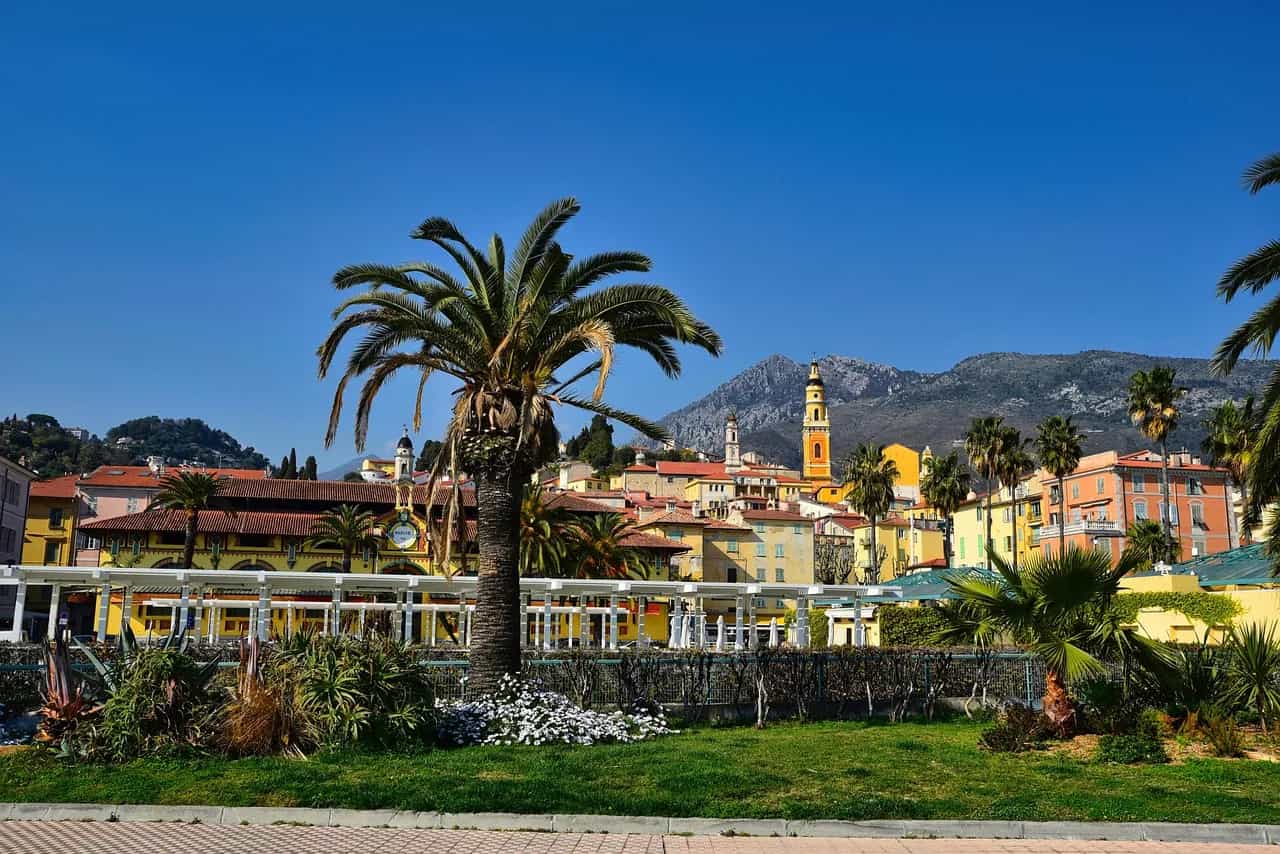 Palm trees and colourful old-town buildings in Menton on the French Riviera, with mountains behind.