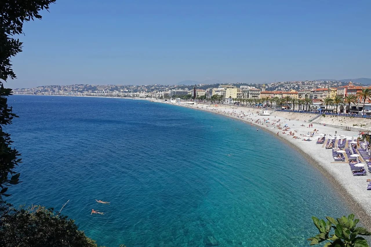 Turquoise water and a curving pebble beach along the French Riviera, with the town stretching into the haze.