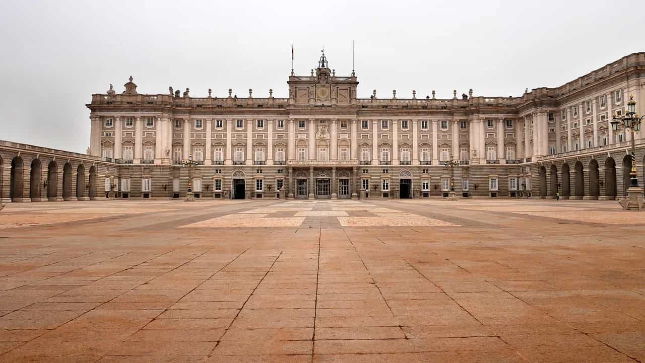The Royal Palace of Madrid across its vast empty stone courtyard under a pale sky.