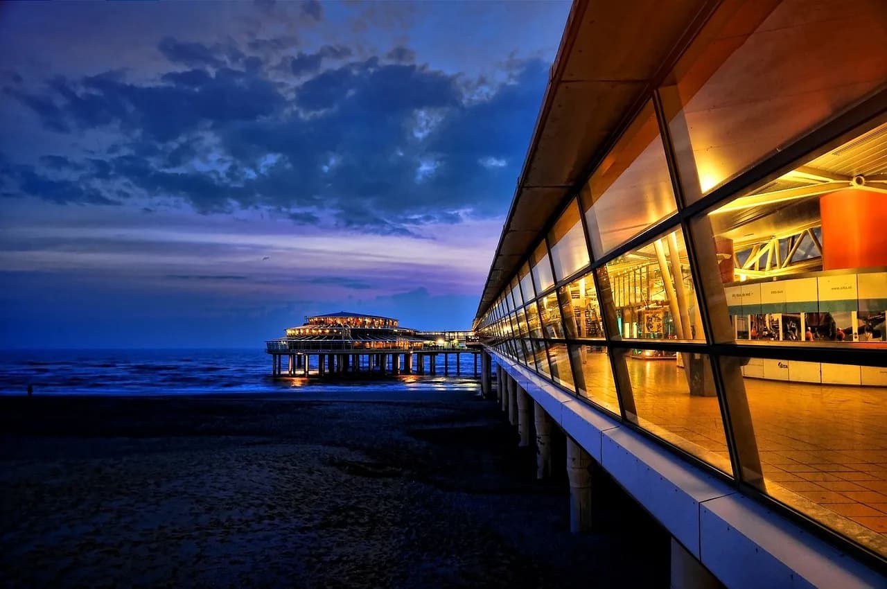 Scheveningen beach and pier lit at dusk under a dramatic North Sea sky.