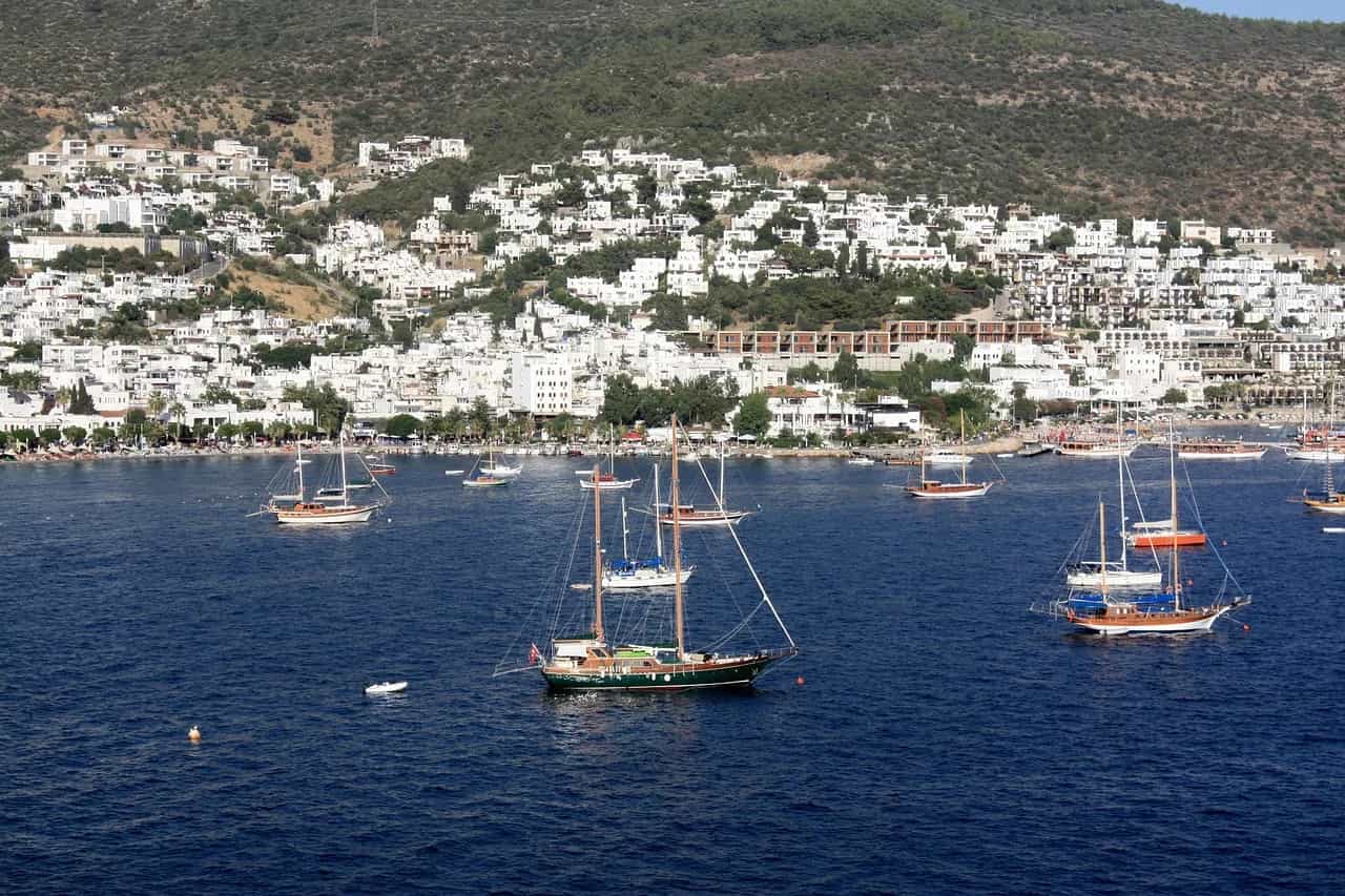 Whitewashed houses climbing the hillside above Bodrum bay, with traditional wooden gulets at anchor.